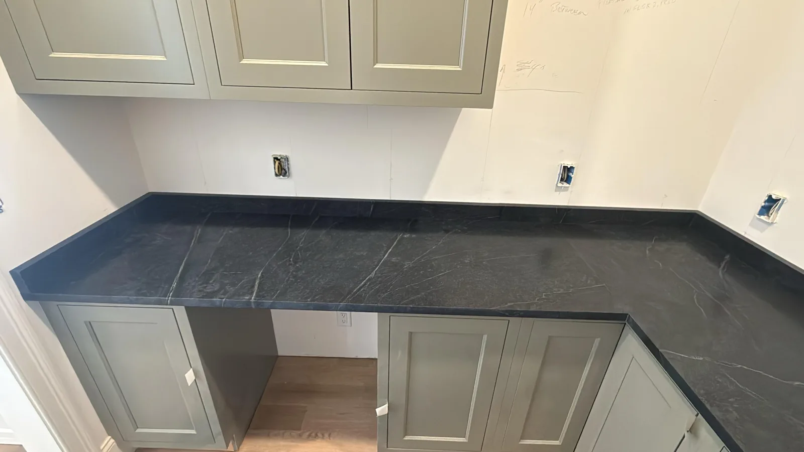 Charcoal soapstone countertops with white veining on sage green cabinets